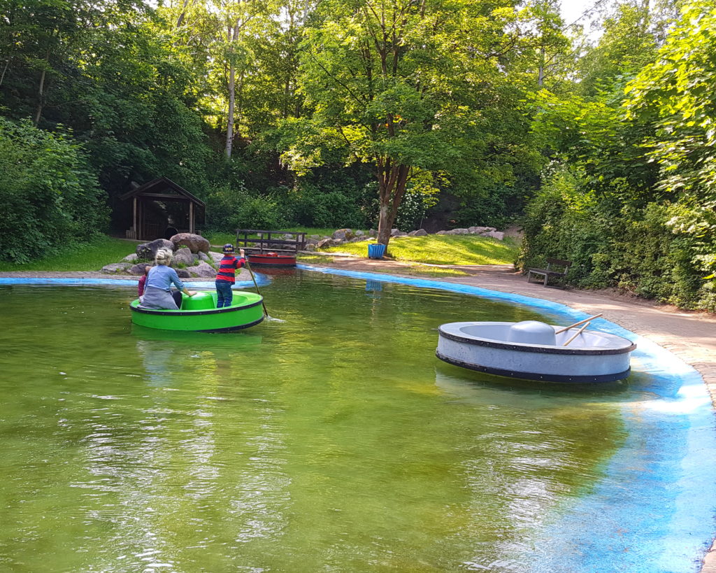 Die Kinder fahren auf dem Floß im Spielpark an der Wingst, im Hintergrund ist das Ende der riesigen Tunnelrutsche zu sehen