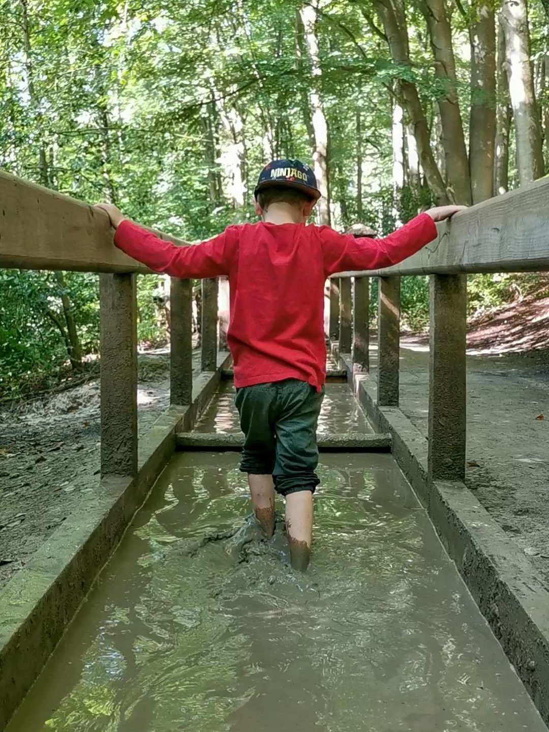 Junge läuft durch ein Wasserbecken auf dem Barfußpfad im Wald